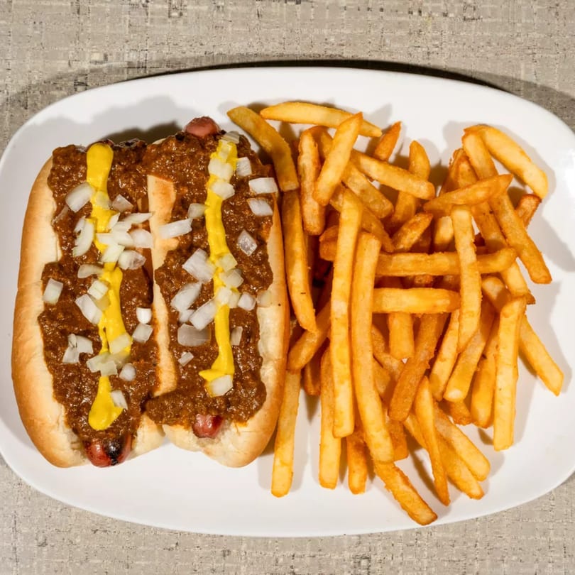Two chili dogs with mustard and diced onions, served with a side of golden french fries.