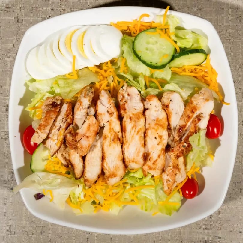 Grilled chicken salad with lettuce, shredded cheese, cucumbers, cherry tomatoes, and sliced hard-boiled eggs.