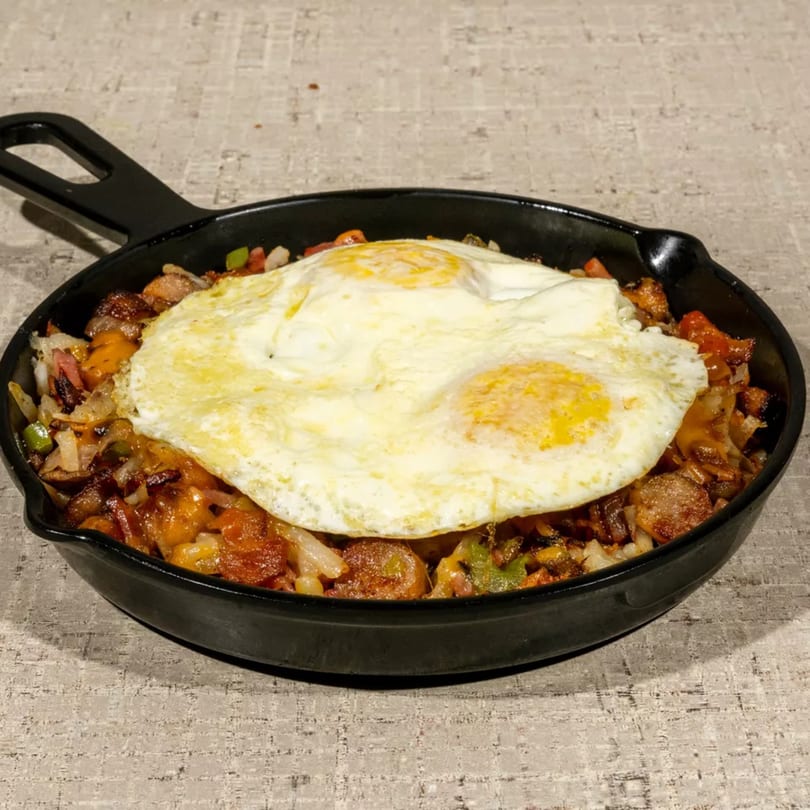 Breakfast skillet with fried eggs, sausage, potatoes, onions, and peppers in a cast iron pan.