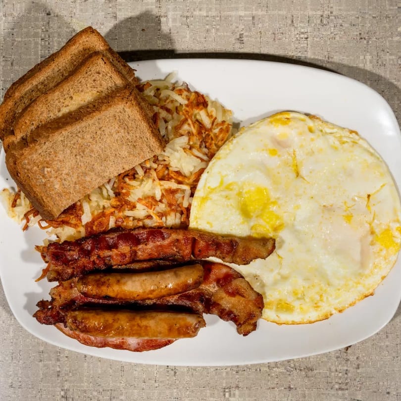 A breakfast plate with fried eggs, hash browns, bacon, sausages, and toast.