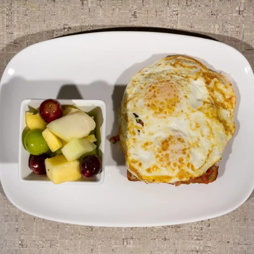 Breakfast plate with fried eggs on toast and a side of fresh fruit salad.