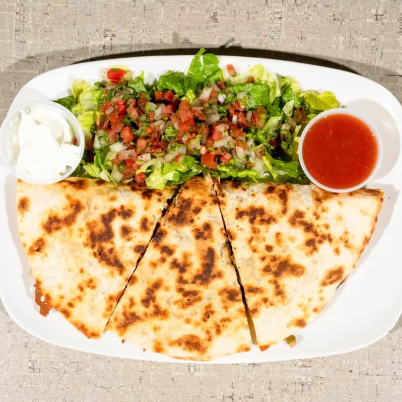 A quesadilla cut into three slices, served with a side salad, sour cream, and salsa.