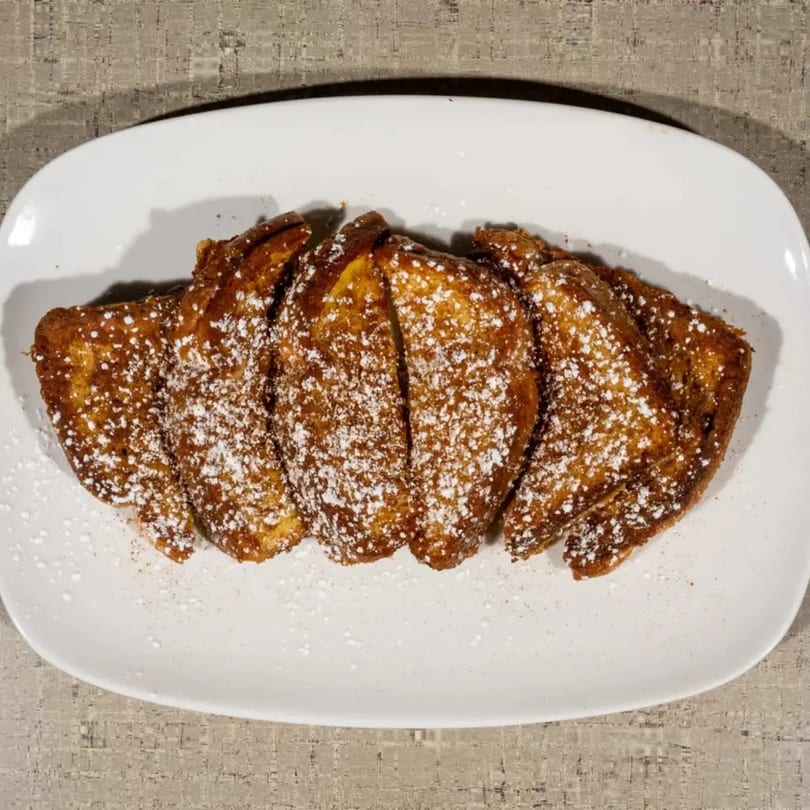 Golden-brown French toast sticks, dusted with powdered sugar, arranged on a white rectangular plate.
